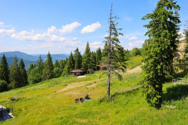 Yeşil yamaçlı dağlık bölge ormanla kaplı, parlak mavi bulutlu ağaçların altında küçük, rahat evler yayılmış ağaçların arasına..