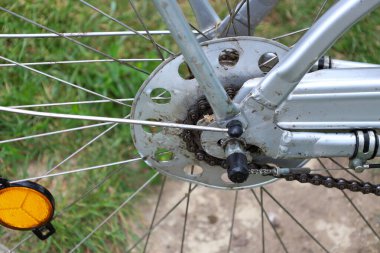 Kirli bir kaset, zincir ve yansıtıcı parıltılı tellerin yer aldığı eski bir bisikletin arka tekerinin yakın plan çekimi. Parçaların yıpranmış durumu sık kullanıldığını ve çok sayıda yolculuk yapıldığını gösterir..