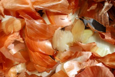 Bir yığın soğan kabuğu, yemek pişirme sürecini ve mutfak işini ön plana çıkarıyor. Parlak ışıklandırmalı kabukların makro görüntüsü dokularını ve doğal renklerini gösterir..