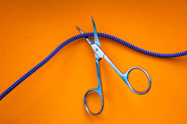 Metal makas parlak turuncu bir zemin üzerinde mavi ve beyaz bir halatı kesiyor, bir mola, bir son ya da özgürlüğü simgeliyor. Bu görüntü, bir karar verme hissini ve hayattaki radikal değişiklikleri aktarıyor..