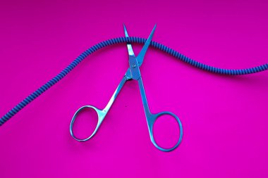 Parlak tıbbi makas, parlak pembe arka planda kırmızı beneklerle mavi kabloyu kesmeye hazırdır. Bu fotoğraf gerilim yaratıyor, karar anı ve potansiyel bir mola gösteriyor..