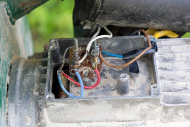 Elektronik bir motor fuarının yakın plan görüntüleri yıpranmış kablolar, terminaller ve pas, teknik ve endüstriyel bir temayı vurguluyor. Metalik doku ve kirli yüzeylerin birleşimi, yaşlılık duygusu ve ekipmanların yoğun kullanımı yaratıyor..