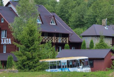 Slavsko, Ukrayna - 13 Temmuz 2025: Bir orman zeminine karşı ahşap süslemeli ve tavan arası pencereli dağlık bir bölgede modern turist kulübeleri. Ön planda, yeşil çimlerin üzerinde duran eski bir otobüs görülebilir..