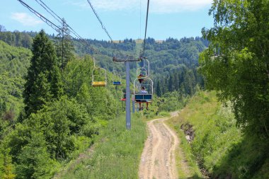 Slavsko, Ukrayna - 13 Temmuz 2025: Mutlu turistler görkemli dağların panoramik manzarasının keyfini çıkararak bir asansöre biniyorlar. Bu resimli ulaşım, dinlenmek ve sık ormanlarla kaplı dağ manzaralarını incelemek için ideal bir yoldur..