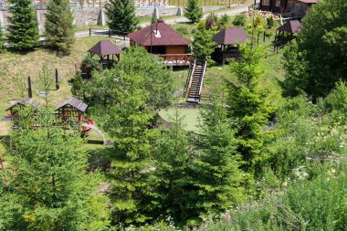Slavsko, Ukrayna - 13 Temmuz 2025: Yeşil bir yamaçta yer alan rahat bir dinlenme tesisi, ahşap çardaklar, bir çocuk parkı ve bir gölet içerir..