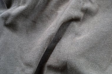 Gri bir kumaşın, sayısız kıvrım ve kırışıklıklarla yakın plan görüntüsü. Yüzeyin ince bir dokuması var, bu da hacmi ve görsel ilgiyi arttırıyor..