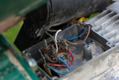 Eski bir mekanizmadaki elektrik bağlantılarına ve kablolara yakın çekim. Çeşitli renkli kablolar, terminaller ve metal parçalar görülebilir, bu da teknik yönünü ve olası tamir ihtiyacını gösteriyor.
