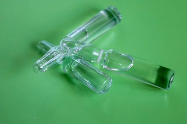 Çeşitli boyutlarda cam ampullerden oluşan bir grup katı yeşil arka planda çapraz yönde uzanır. Bu fotoğraf ilaç ürünlerini, laboratuvar araştırmalarını ve tıbbi ekipmanları, tedaviyi ve bilimi sembolize ediyor..