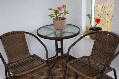 Hasır sandalyeli küçük bir oturma odası ve cam kapaklı yuvarlak bir masa. Balkon ya da verandada vakit geçirmek için rahat bir yer yaratıyor..