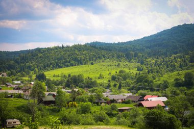 Yeşil tepeler ve sık ormanlarla çevrili bir vadideki küçük bir köyün açık manzarası. Fotoğraf, huzurlu bir yaşam atmosferi, doğa ile uyum ve kırsal cennet taşır..