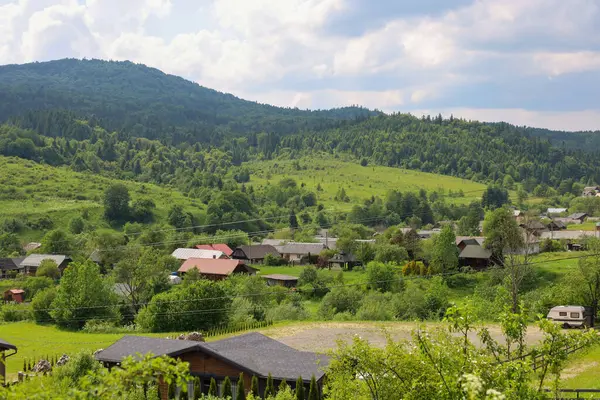 Orman dağlarının yeşilliği ve vadideki sıcacık evlerle dolu kırsal bir Karpatya manzarası. Parlak güneş tepeleri aydınlatır ve barış ve doğanın uyumlu bir atmosferini yaratır..