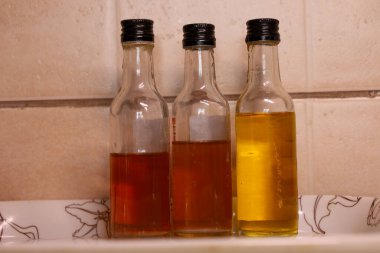 Üç küçük cam şişe koyu kapaklı dekoratif bir tepside yan yana durur, farklı renk yoğunluğundaki yağlar ve tentürlerle doludur..