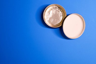 Two round metal lids or bottoms of small tins lie in the upper right corner on a bright blue background, leaving most of the frame for empty space.