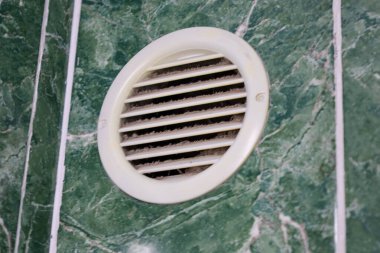 Bu yakın çekim, yeşil mermer desenli fayans duvarına monte edilmiş toz ve toprakla tıkanmış yuvarlak plastik bir havalandırma ızgarası içeriyor..