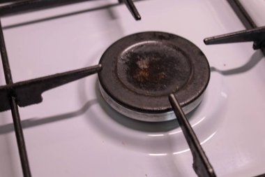 Bu detaylı yakın plan temiz beyaz bir gaz sobasının tek bir ocağına odaklanıyor, dökme demir ızgarayı ve metal yakıcı kapağı gösteriyor..