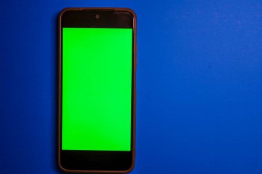 Bu fotoğraf ekranın değiştirilmesi ya da mobil bir uygulama ya da video içeriğine metin / görüntü eklemek için mükemmeldir. Parlak yeşil ekranlı bir akıllı telefon doymuş mavi bir arkaplanda duruyor ve güçlü bir renk kontrastı oluşturuyor.