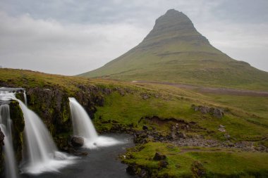 Kirkjufellsfoss şelalesinin tepesinde Kirkjufell dağının arka planında İzlanda 'nın kuzey kıyısında uzun bir kepenk indirme hızı ile çekilmiştir.