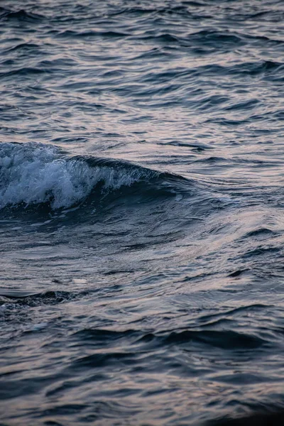 日没時に海の波が打ち寄せられ 水面からのオレンジ色の光が反射する — ストック写真
