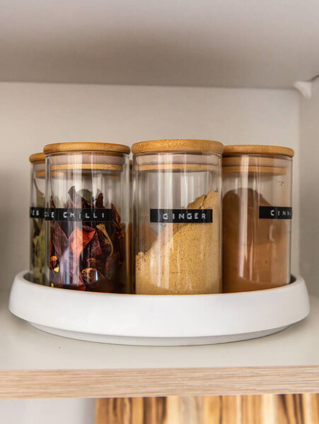 Neatly organized labeled food pantry in a home kitchen with spices in glass wooden spice jars
