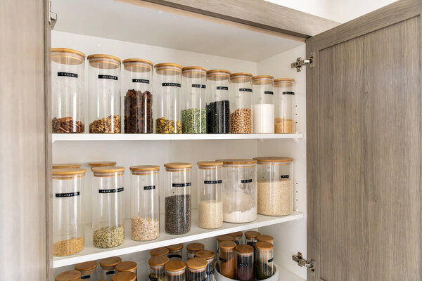 Neatly organized labeled food pantry in a home kitchen with spices grains flour rice sugar nuts