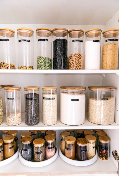 Neatly organized labeled food pantry in a home kitchen with spices in glass wooden spice jars