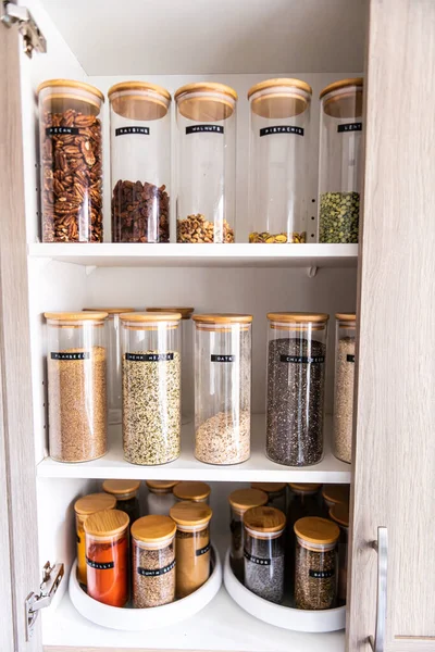 Neatly organized labeled food pantry in a home kitchen with spices in glass wooden spice jars