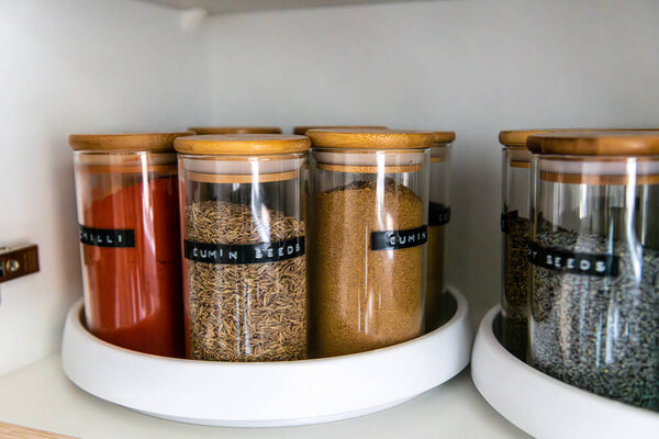 Neatly organized labeled food pantry in a home kitchen with spices in glass wooden spice jars
