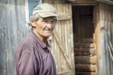 Yazın güneşli bir günde, kırsal alanda duran, beyzbol şapkalı ve kısa kollu tişörtlü yaşlı bir adamın portresi. Köy hayatı, yaşlılık..