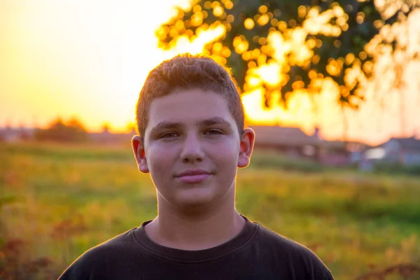 stock image In the summer in the village in the garden at sunset, a teenage boy stands.