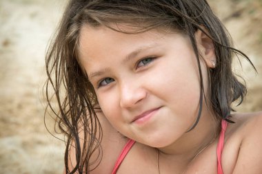 Kumsalda oturan, ıslak saçlı, sevimli, çocuksu duyguları olan, mutlu bir kız. Yaz tatili konsepti. Tatlı kız yaz tatilinde eğleniyor..