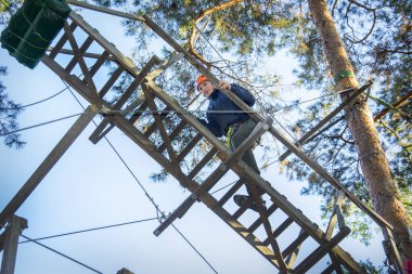Aşırı bir parkta teleferiğe bir çocuk. Bir çocuk koruyucu kask ve sigorta giyinmiş, teleferiğe engellerin üstesinden gelir.