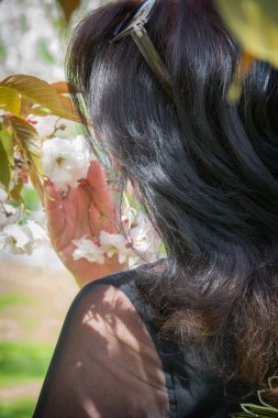 Sakura yakınlarında bir kadın. Çiçek açan ağaçlı bir kız. Uzun saçlı güzel bir kadın portresi. Duygusal bir kadın. Nazik kız. Bakım, portre. Güzel gülümseme.