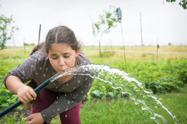 Yaz öğleden sonra bahçede, bir kız hortumdan su içer..