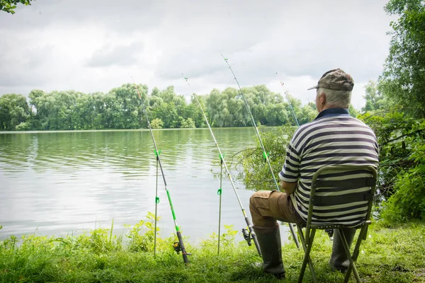 stock image In summer, an adult man sits near the river and catches fish.