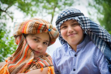 Erkek ve kız kardeş yazın Hindu ve Arap kostümü giyer. Şapkalı bir kız ve Arafatlı bir oğlan..