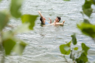 Yazın, erkek ve kız kardeş nehirde yıkanır. Ağaçların yapraklarından onları görebilirsin..