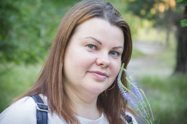 Parkta mutlu bir kadının yakın çekimi elinde bir buket kır çiçeğiyle gün ışığında duruyor..