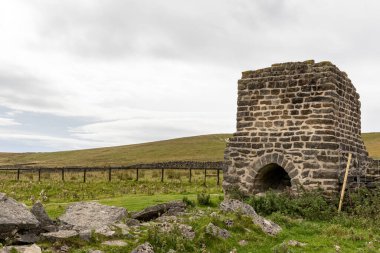 Arka planda bulutlu bir gökyüzü olan taştan bir duvarın dikey görüntüsü.