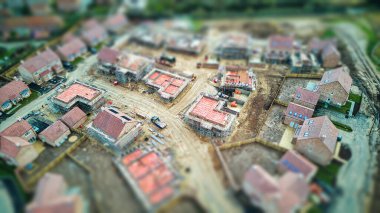 Kısmen inşa edilmiş evleri ve toprak yolları olan bir inşaat alanının havadan görünüşü, minyatür bir görünüm için eğim kayması etkisi kullanıyor..