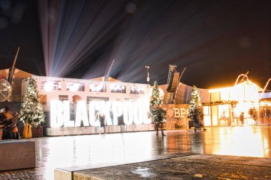 Blackpool Aydınlatmaları 'nın gece görüşü. Parlak ışıklar ve ıslak kaldırımlardaki yansımalar, neşeli bir atmosfer yaratıyor..