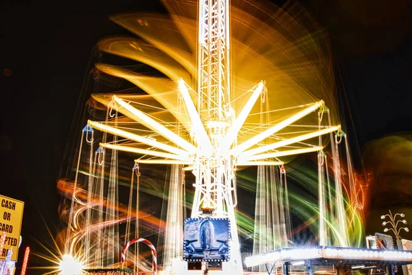 Long exposure of a brightly lit carousel at night, capturing motion blur of spinning lights at a fair.
