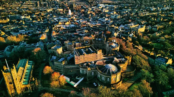 Aerial view of a historic Lancaster castle amidst a sprawling cityscape during golden hour, showcasing architectural beauty and urban density.