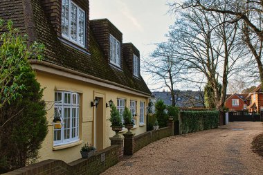 Sarı cepheli, beyaz pencereli ve saksı bitkilerli, sakin bir mahalleye kurulmuş geleneksel İngiliz yazlığı..
