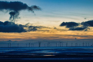 Türbin siluetleri ve dramatik bulutlarla dolu sakin bir rüzgâr çiftliğinde gün batımı Crosby, İngiltere 'de suyu yansıtıyor..