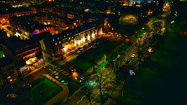 Aerial night view of a lit-up urban street with rows of buildings and trees in Harrogate, North Yorkshire.