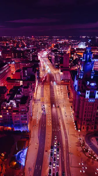 Vertical aerial view of a bustling city street at night with vibrant purple lighting and traffic trails in Liverpool, UK.