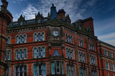 Leeds, İngiltere 'de karamsar bir gökyüzünün altında saat kulesi olan Gotik tarzı kırmızı tuğla bina..