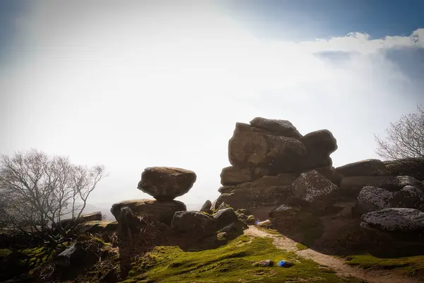 Misty landscape with balancing rock formations and a clear path under a bright sky at Brimham Rocks, in North Yorkshire