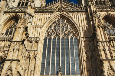 Bir katedralin ön cephesinin Gotik mimari ayrıntıları, büyük bir vitraylı pencere ve York, Kuzey Yorkshire, İngiltere 'de açık gökyüzünün altında süslü taş oymalar içeriyor..