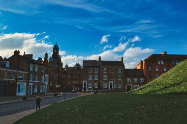 Tüylü bulutlu dramatik mavi gökyüzü altında tarihi binaları olan tuhaf Avrupa kasabası, New York, Kuzey Yorkshire, İngiltere 'de bir kaldırımda yemyeşil bir tepe ve yayalar bulunuyor..